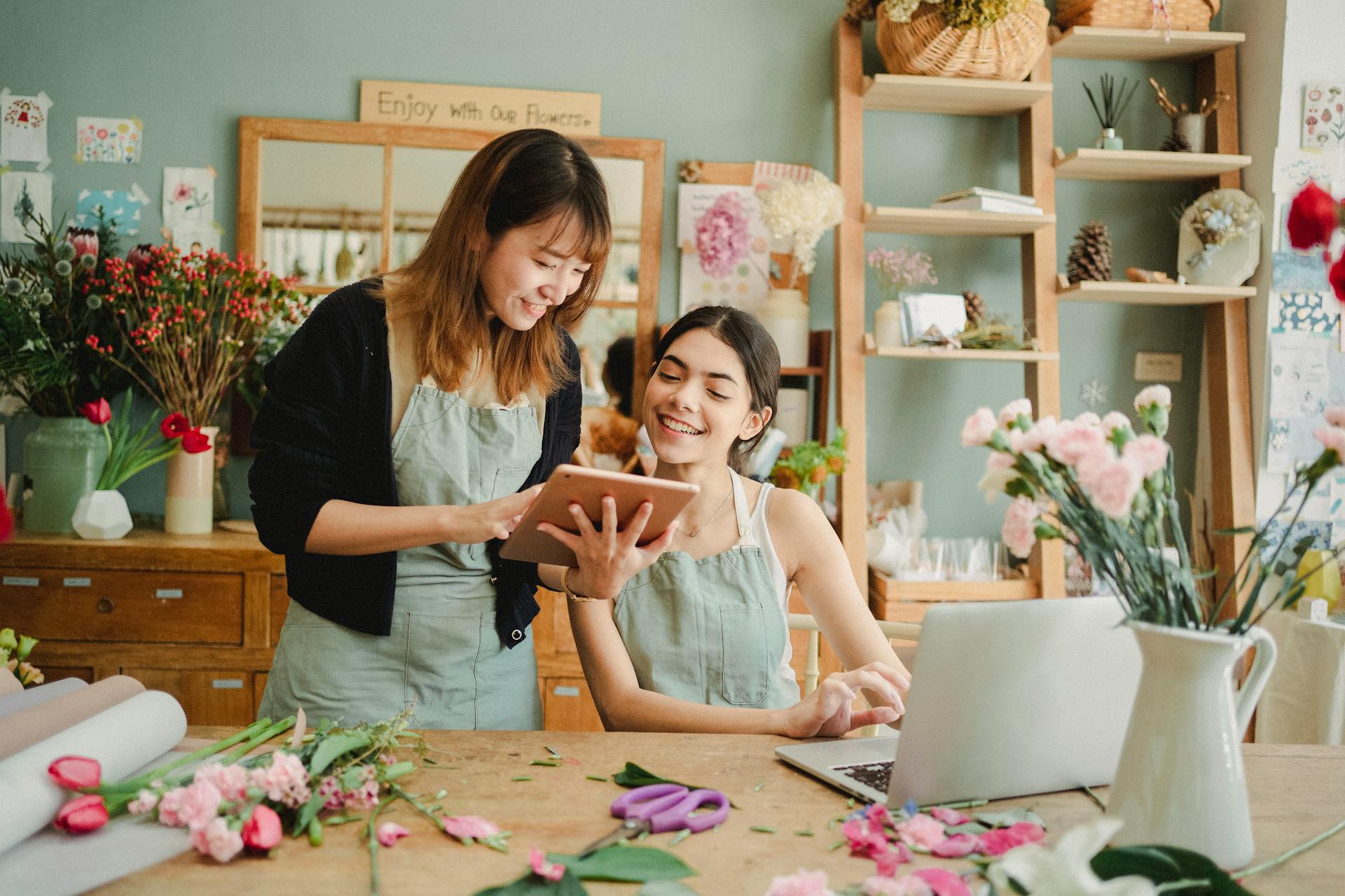 Two women in a flower shop looking at a laptop and notebook